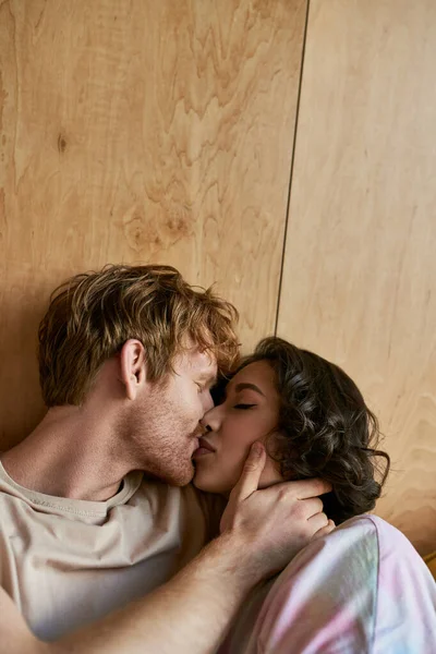 Momento íntimo de casal multicultural, feliz ruiva homem com olhos fechados beijando mulher asiática — Fotografia de Stock