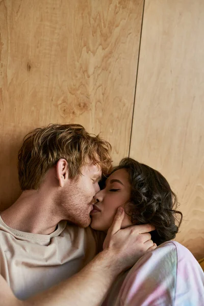 Intimate moment of multicultural couple, happy redhead man with closed eyes kissing asian woman — Stock Photo