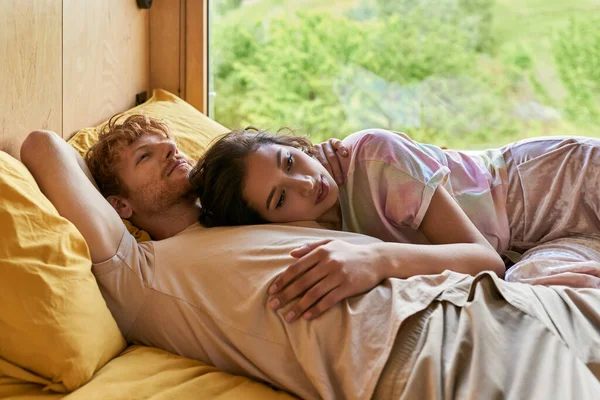Sensual asian woman lying on belly of redhead boyfriend, waking up together in country house — Stock Photo