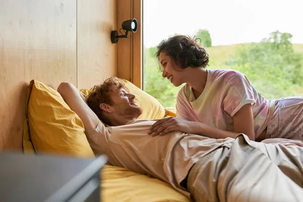 Happy asian woman looking at redhead boyfriend, interracial couple waking up in country house — Stock Photo