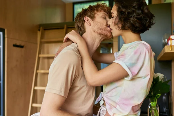 Affectueux interracial couple baisers à la maison, jeune rousse homme et asiatique femme en amour — Photo de stock
