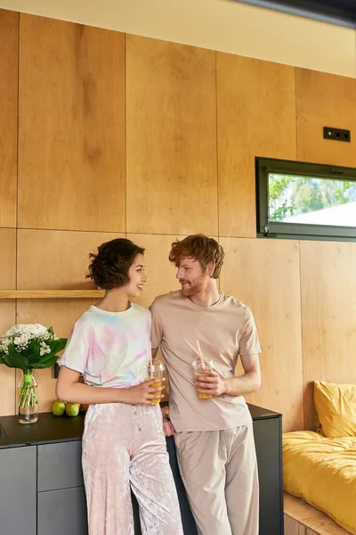 Glückliches multikulturelles Paar, das morgens im Pyjama steht und Gläser mit Orangensaft in der Hand hält — Stockfoto