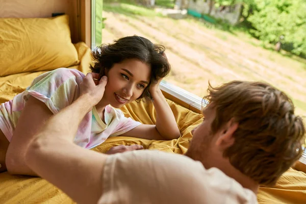 Tender gesture, redhead man touching cheek of asian woman and lying on bed together in morning — Stock Photo