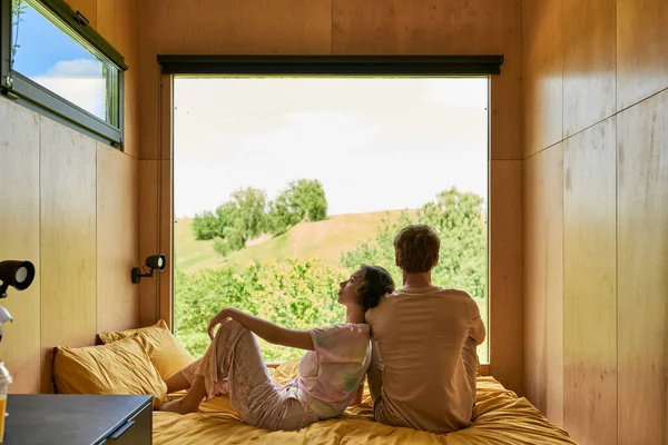 Азиатская женщина сидит на кровати и опираясь на плечо бойфренда, расслабляясь вместе в загородном доме — стоковое фото