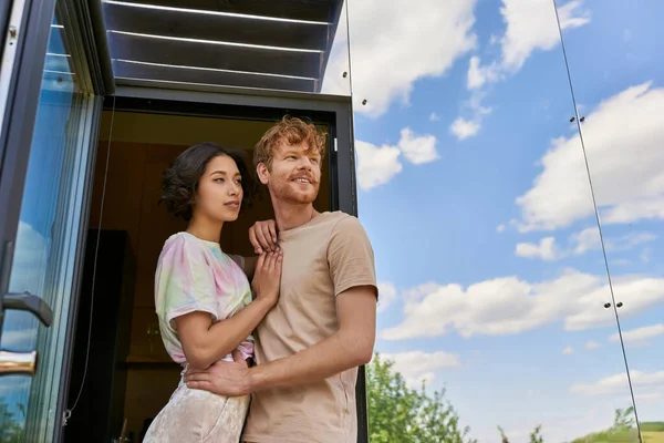 Dreamy interracial couple standing at front door of modern glass house and looking away, fresh air — Stock Photo