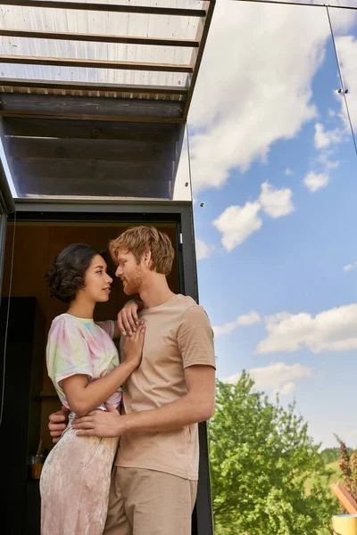 Affectionate interracial couple standing at front door of glass house and looking at each other — Stock Photo