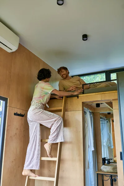 Heureux rousse homme regardant brunette copine grimper sur échelle de lit superposé, week-end escapade — Photo de stock