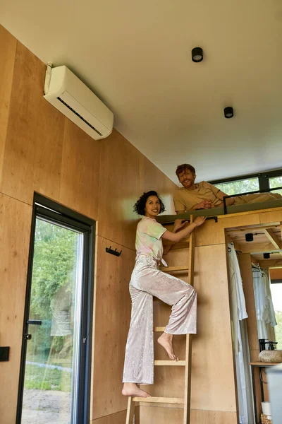 Heureux rousse homme regardant caméra tandis que petite amie grimpant sur l'échelle de lit superposé, week-end escapade — Photo de stock