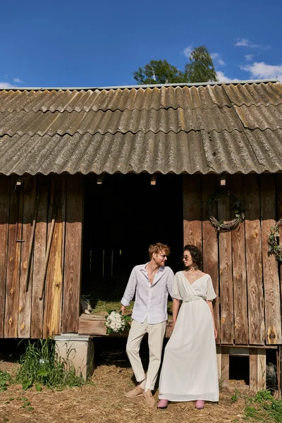 Rustic wedding concept interracial newlyweds in sunglasses and wedding gown near wooden barn — Stock Photo