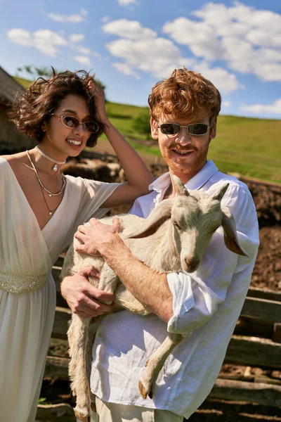 Rustic wedding in boho style, happy man holding baby goat near young asian woman  in wedding dress — Stock Photo