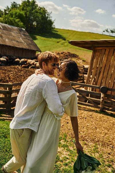 Boda rústica en estilo boho, novia asiática interracial abrazando novio cerca de ganado en granja - foto de stock