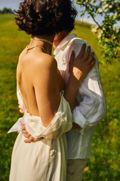 Sposa bruna in abito bianco in piedi con sposo in giardino verde, sposi novelli in campagna — Foto stock