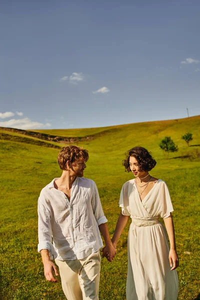 Wedding in countryside, multiethnic couple holding hands in green field, just married newlyweds — Stock Photo