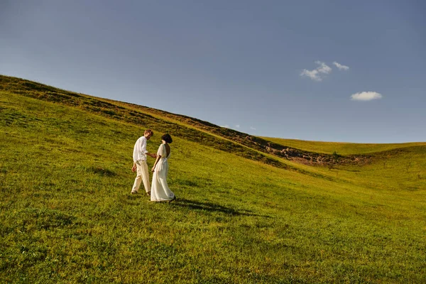 Beautiful landscape, just married couple walking in green field, young newlyweds in wedding gown — Stock Photo