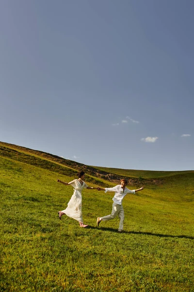 Scenic landscape, young newlyweds in wedding gown running in green field, just married couple — Stock Photo