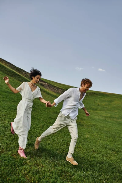 Candid photo, happy young newlyweds in wedding gown running in green field, just married couple — Stock Photo