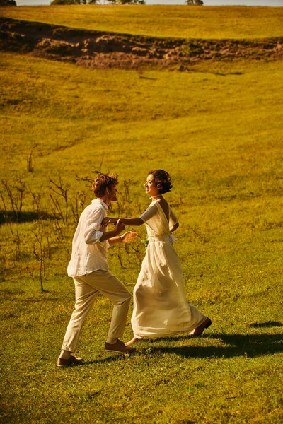 Playful interracial newlyweds in wedding attire having fun in green field, rustic wedding — Stock Photo