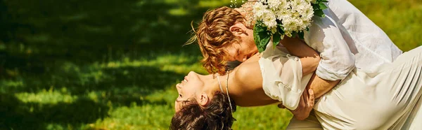 Joven pelirroja hombre abrazando y besando asiático mujer con boda bouquet al aire libre, bandera - foto de stock