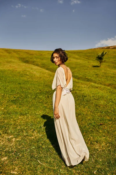 Young asian woman in white wedding dress looking at camera in field under blue sky, full length — Stock Photo