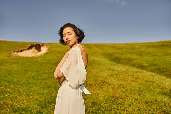 Morena asiática mulher no boho estilo vestido de noiva olhando para a câmera no campo verde no campo — Fotografia de Stock