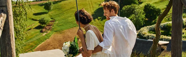 Felice coppia appena sposata in stile boho abbigliamento divertirsi sull'altalena in un tranquillo ambiente rurale, banner — Foto stock