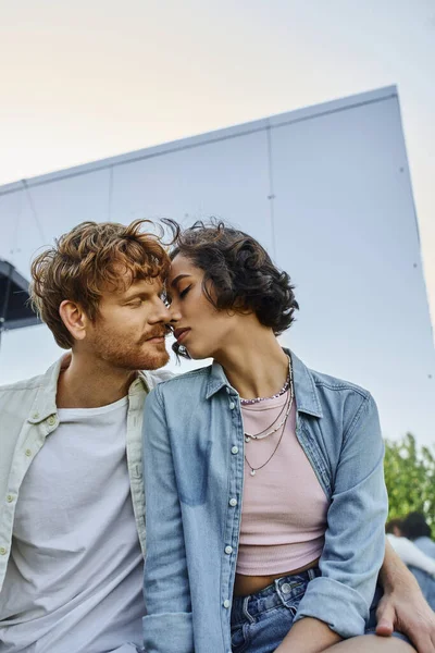 Rothaarige Mann und junge asiatische Frau küssen sich mit geschlossenen Augen in der Nähe von Glashaus, Liebe und Zärtlichkeit — Stockfoto