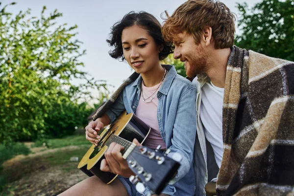 Jeune femme asiatique jouer de la guitare acoustique à heureux rousse copain pendant la date dans la campagne — Photo de stock