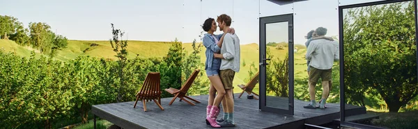 Interracial couple hugging on porch near modern glass house, romantic date in countryside, banner — Stock Photo