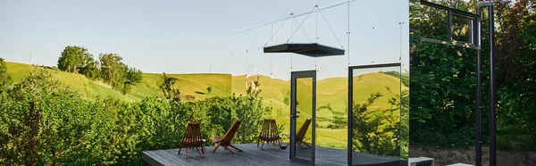 Moderna casa de cristal con sillas en el porche de madera, entorno rural tranquilo, pancarta - foto de stock