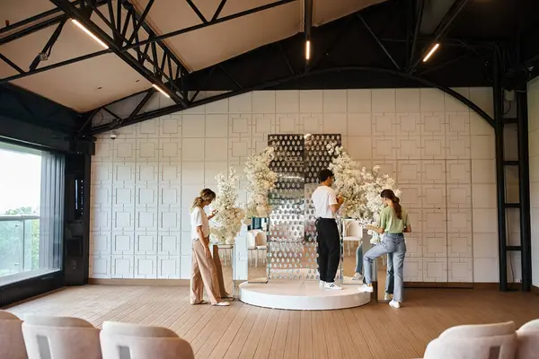 Grupo de decoradores que decoran la moderna sala de eventos con flores blancas, trabajo en equipo y preparación de eventos - foto de stock