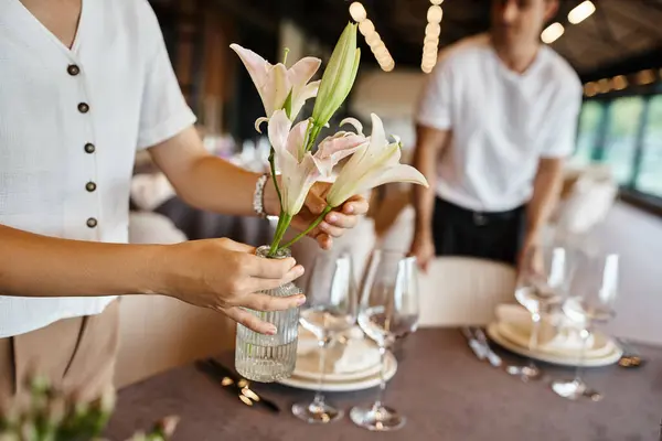 Vue recadrée du décorateur tenant vase et fleurs près de la table avec cadre festif dans la salle des événements — Photo de stock