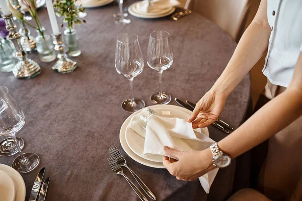Cropped view of woman arranging festive table setting and holding napkin near plates, event styling — Stock Photo