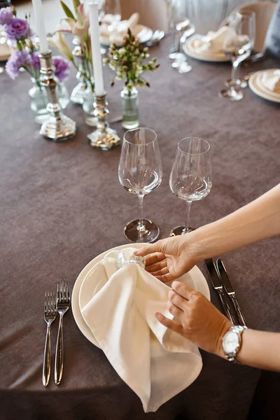 Обрізаний вид декоратора, що тримає серветки біля тарілок на столі зі святковою обстановкою, налаштування подій — стокове фото