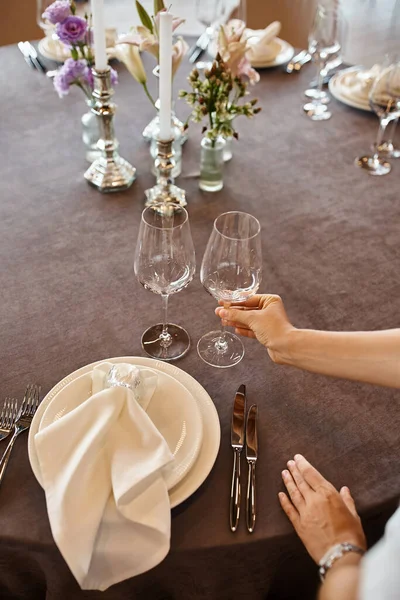 Cropped view of event decorator holding glass near table with festive setting, banquet setup — Stock Photo