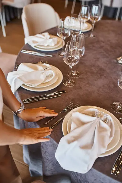 Vista recortada del decorador que organiza el banquete en la mesa con decoración floral en la sala de eventos moderna - foto de stock