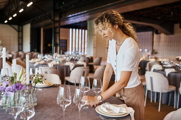 Mulher com cabelo ondulado colocando óculos na mesa com ambiente festivo, coordenador do banquete no trabalho — Fotografia de Stock