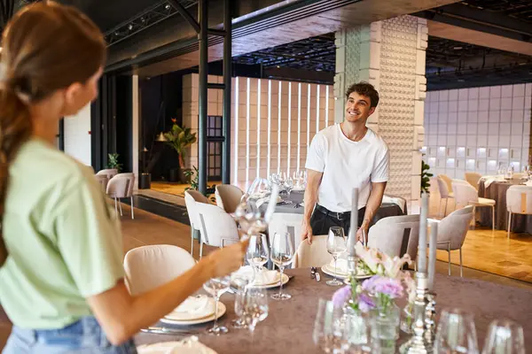 Homem sorridente perto de mesas festivas olhando para a mulher em primeiro plano borrado, organizadores do banquete no trabalho — Fotografia de Stock