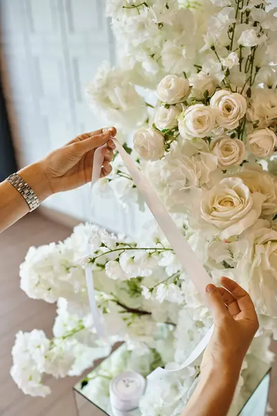 Vista parziale del decoratore che tiene il nastro bianco vicino ai fiori in fiore nella sala banchetti, allestimento eventi — Foto stock
