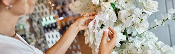 Cropped view of decorator tying ribbon on white floral composition in festive event hall, banner — Stock Photo