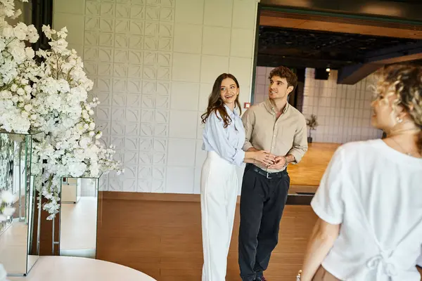 Casal espantado olhando para a composição floral branca perto do gerente de eventos no salão de banquetes moderno — Fotografia de Stock