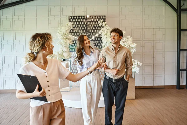Professioneller Eventmanager mit Klemmbrett, das Hochzeitslocation mit floralem Dekor für glückliches Paar zeigt — Stockfoto