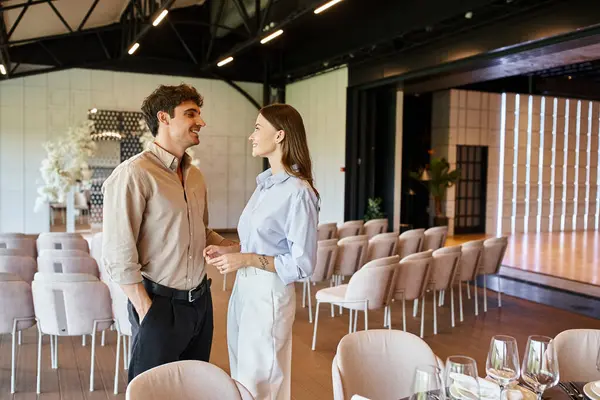 Casal sorrindo falando perto da mesa festiva com o cenário do banquete no salão de eventos com decoração de casamento — Fotografia de Stock