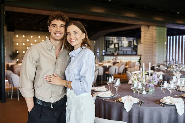 Couple heureux en amour regardant la caméra dans la salle de banquet avec des tables de fête décorées, jour spécial — Photo de stock