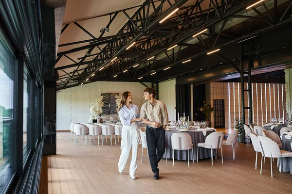 Счастливая влюбленная пара прогуливаясь по банкетному залу со свадебным декором и праздничными столами, особенный день — стоковое фото