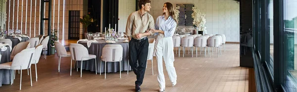 Feliz pareja caminando a lo largo del lugar de la boda con mesas decoradas, preparación del día especial, bandera - foto de stock