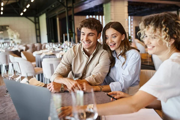 Impressed couple looking at laptop near banquet organizer at festive table in wedding venue — Stock Photo