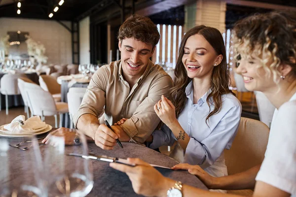 Positive couple signing contract with smiling event manager at festive table in modern event hall — Stock Photo