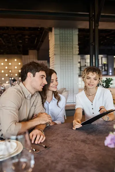 Bankettkoordinator zeigt glücklichem Paar Vertrag, während es am festlichen Tisch im Veranstaltungssaal sitzt — Stockfoto