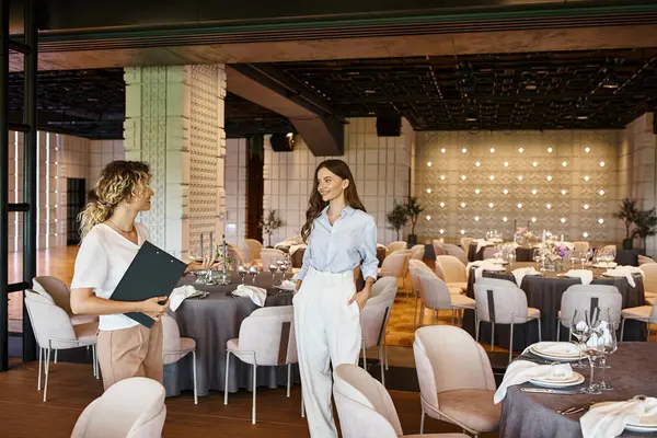 Event coordinator with clipboard showing modern banquet hall with decorated tables to young woman — Stock Photo