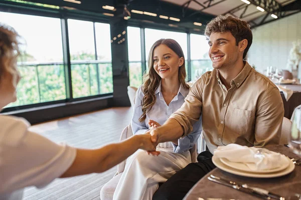 Glücklicher Mann beim Händeschütteln mit Eventkoordinator neben zufriedener Freundin in modernem Hochzeitslokal — Stockfoto